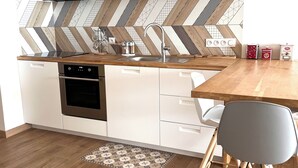 A modern kitchen with white cabinetry, a wooden countertop, a built-in oven, and a herringbone-patterned backsplash. - Apartment with panoramic view of the Sanguinary Islands (Ajaccio)