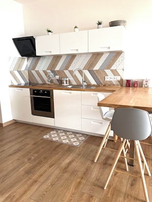 Une cuisine moderne avec des meubles blancs, un plan de travail en bois, un four encastré et un dosseret décoré d’un motif en chevrons.