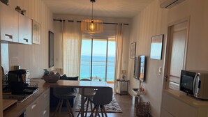 A modern kitchen with a dining area, large windows with a view of the sea, and a ceiling light fixture. - Apartment with panoramic view of the Sanguinary Islands (Ajaccio)