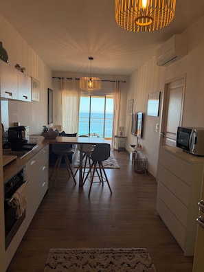 Une cuisine moderne avec un coin repas, de grandes fenêtres offrant une vue sur la mer et un luminaire au plafond.