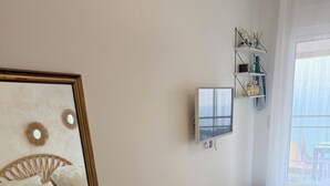 A bedroom with a large mirror, a bed, a bedside table, a wall-mounted shelf with decorative items, and a window with a view. - Apartment with panoramic view of the Sanguinary Islands (Ajaccio)