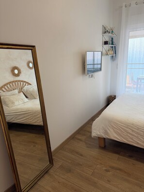 Une chambre avec un grand miroir, un lit, une table de chevet, une étagère murale décorative et une fenêtre donnant sur un beau paysage.