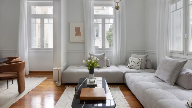 A modern living room with a sofa, a coffee table, and a chair. There is a window with curtains, a picture on the wall, and a vase with flowers on the coffee table. - Beautiful Acropolis Villa 3BR 9ppl 10 minutes Metro&Museum (Athina)