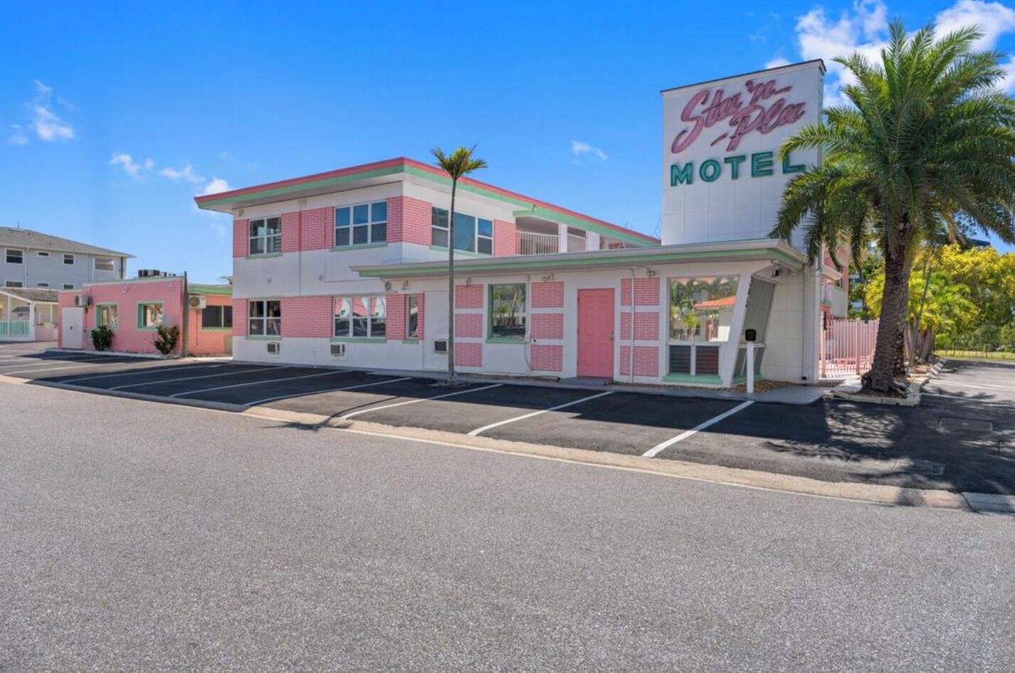 Un motel à la façade rose et blanche, avec une grande enseigne indiquant « Star’s Place Motel », et un parking situé devant.