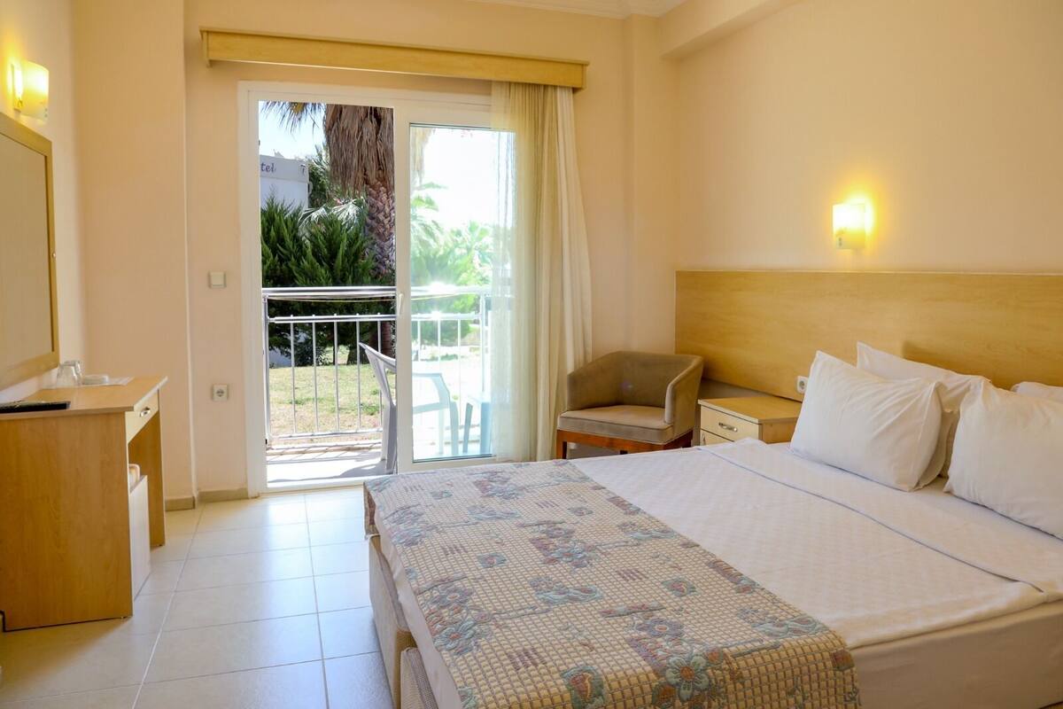 A hotel room with a bed, a desk, a chair, and a balcony with a view of greenery.