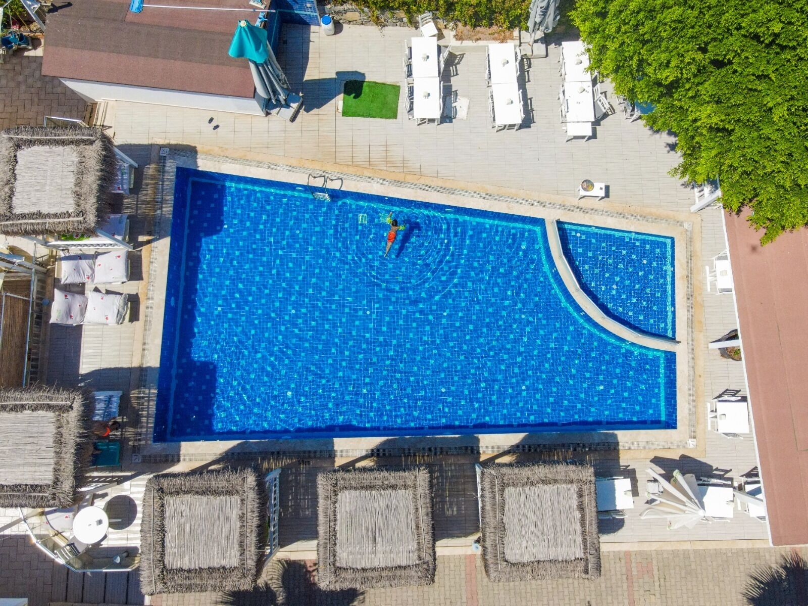 An aerial view of a rectangular swimming pool with a curved section, surrounded by lounge chairs and umbrellas.