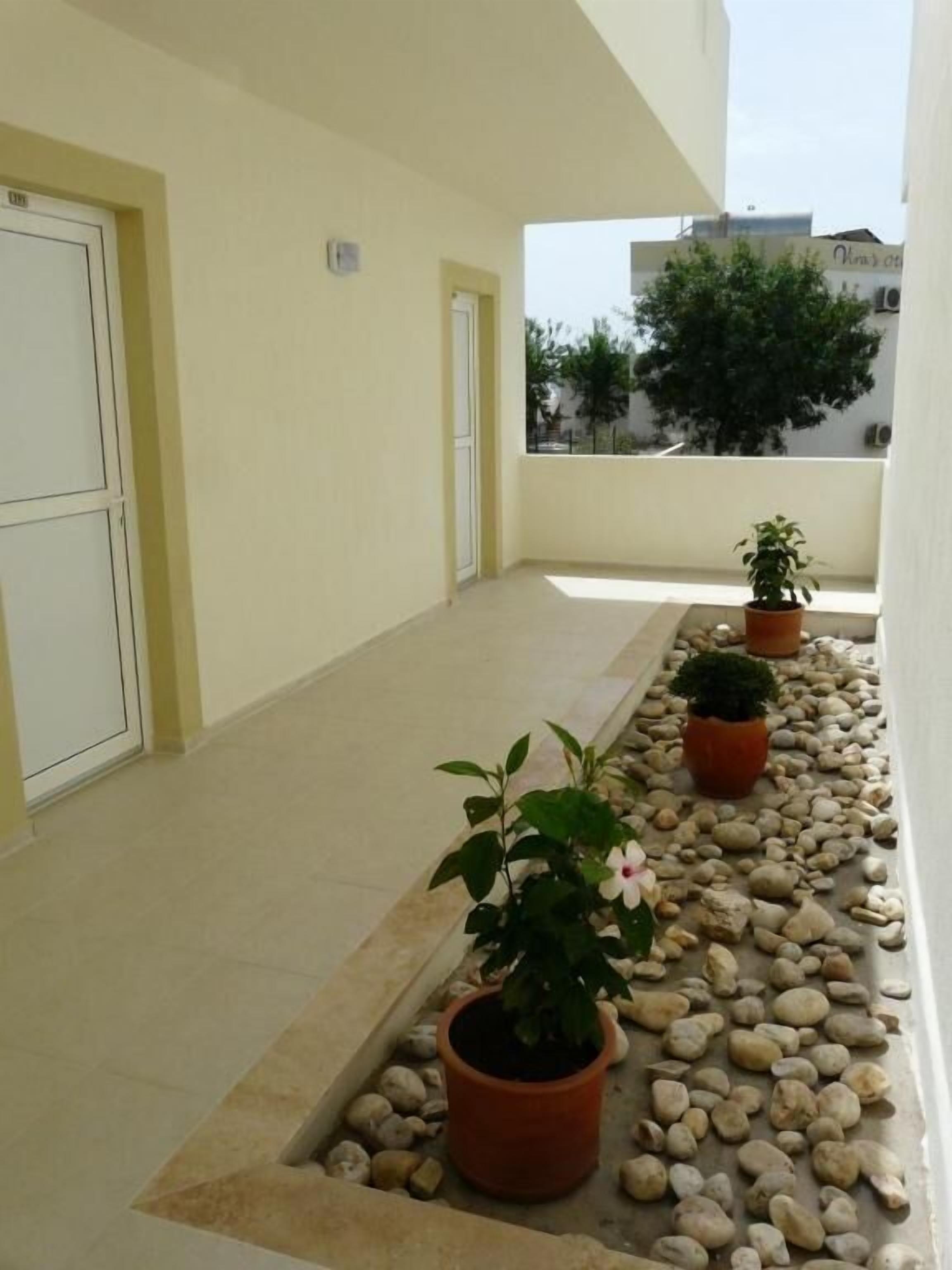 Un pasillo estrecho con suelo de baldosas, plantas en macetas y una zona de grava.