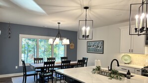 A modern kitchen with a central island, pendant lighting, and a view of the outdoors through large windows.