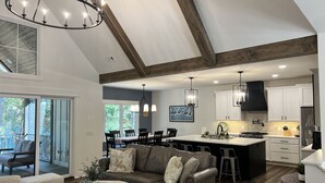 A spacious living room with a large couch, a dining area, and a kitchen with white cabinets and a black stove.