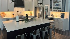 A modern kitchen with a large island, bar stools, stainless steel appliances, and pendant lighting.
