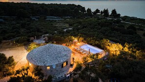 A circular stone building with a swimming pool, surrounded by trees and a view of the sea. - Island Getaway Heritage House: Historical Villa with Heated Pool & Sea Views (Supetar)