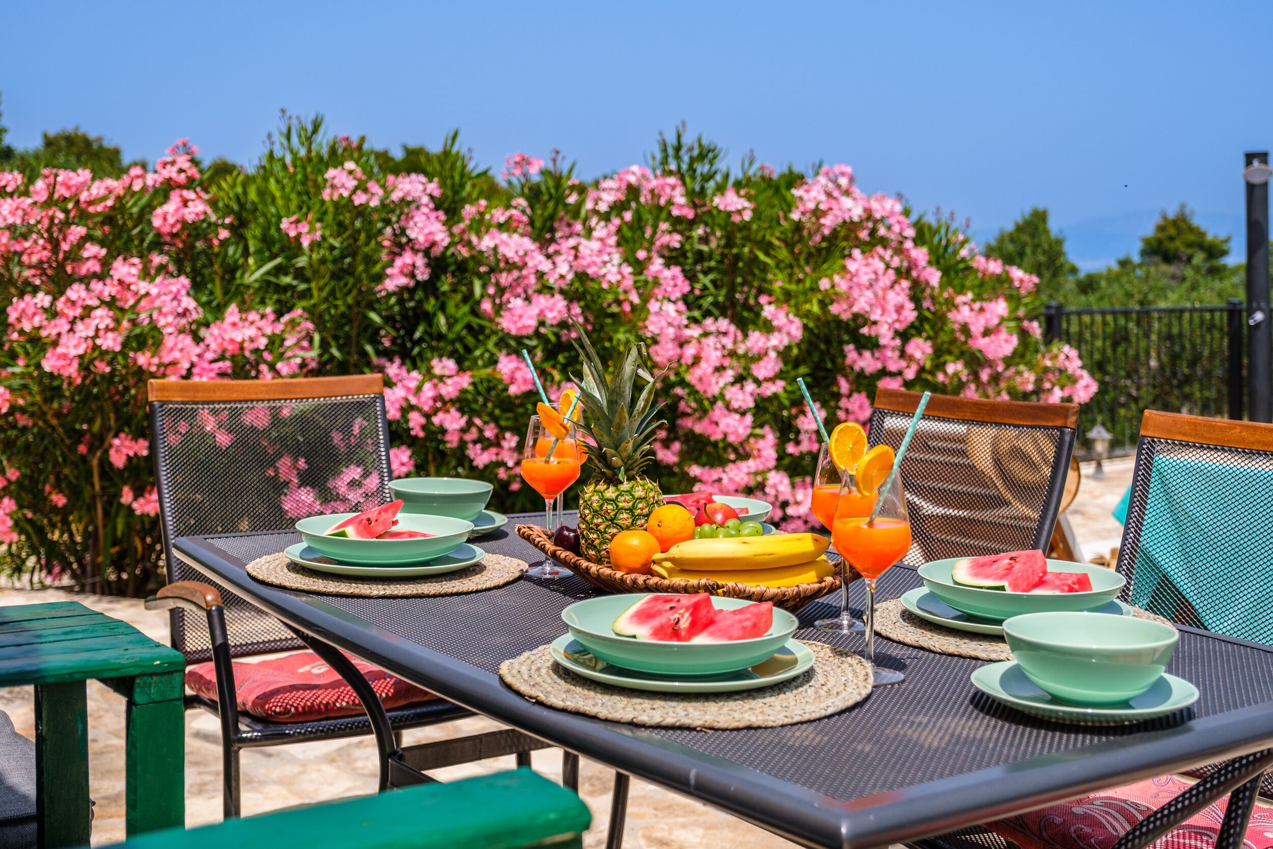 An outdoor dining area with a table set for two, featuring plates, bowls, and a fruit basket.
