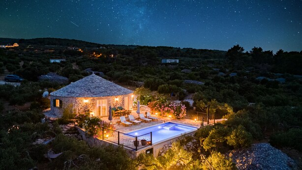 A stone house with a swimming pool surrounded by lush vegetation. - Island Getaway Heritage House: Historical Villa with Heated Pool & Sea Views (Supetar)