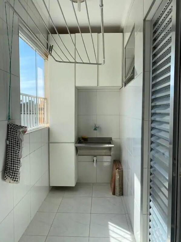 Eine kleine, saubere Küche mit weißen Fliesen, einem Spülbecken und einem Fenster mit Blick.