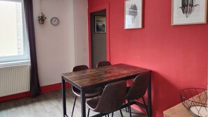 A dining area with a wooden table and four chairs, a red wall, and two framed pictures.