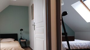 A bedroom with a sloped ceiling, a bed, a desk with a lamp, and a window.