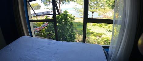 Una cama con vista a un jardín y una masa de agua a través de grandes ventanales.