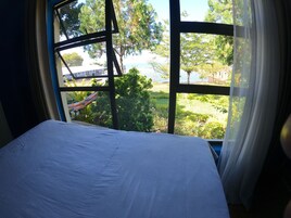 Una cama con vista a un jardín y una masa de agua a través de grandes ventanales.