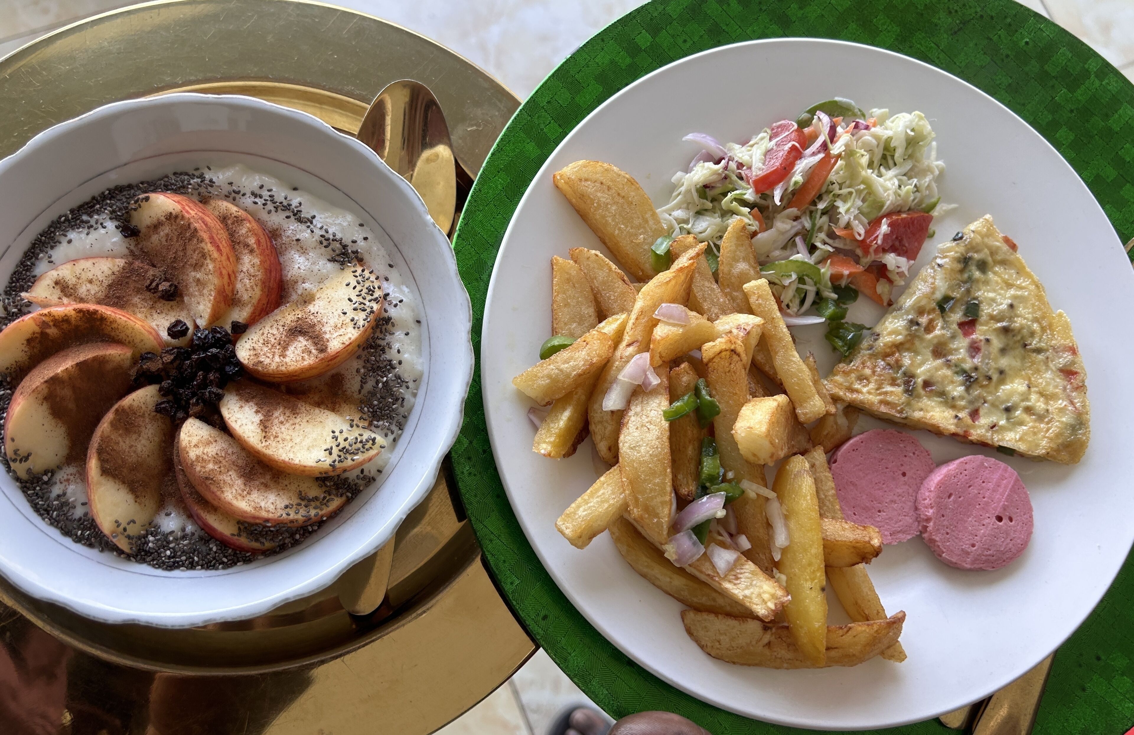 Due piatti di cibo: uno con yogurt guarnito con fettine di mela e semi, l'altro con patatine fritte, insalata di cavolo e una fetta di pizza.