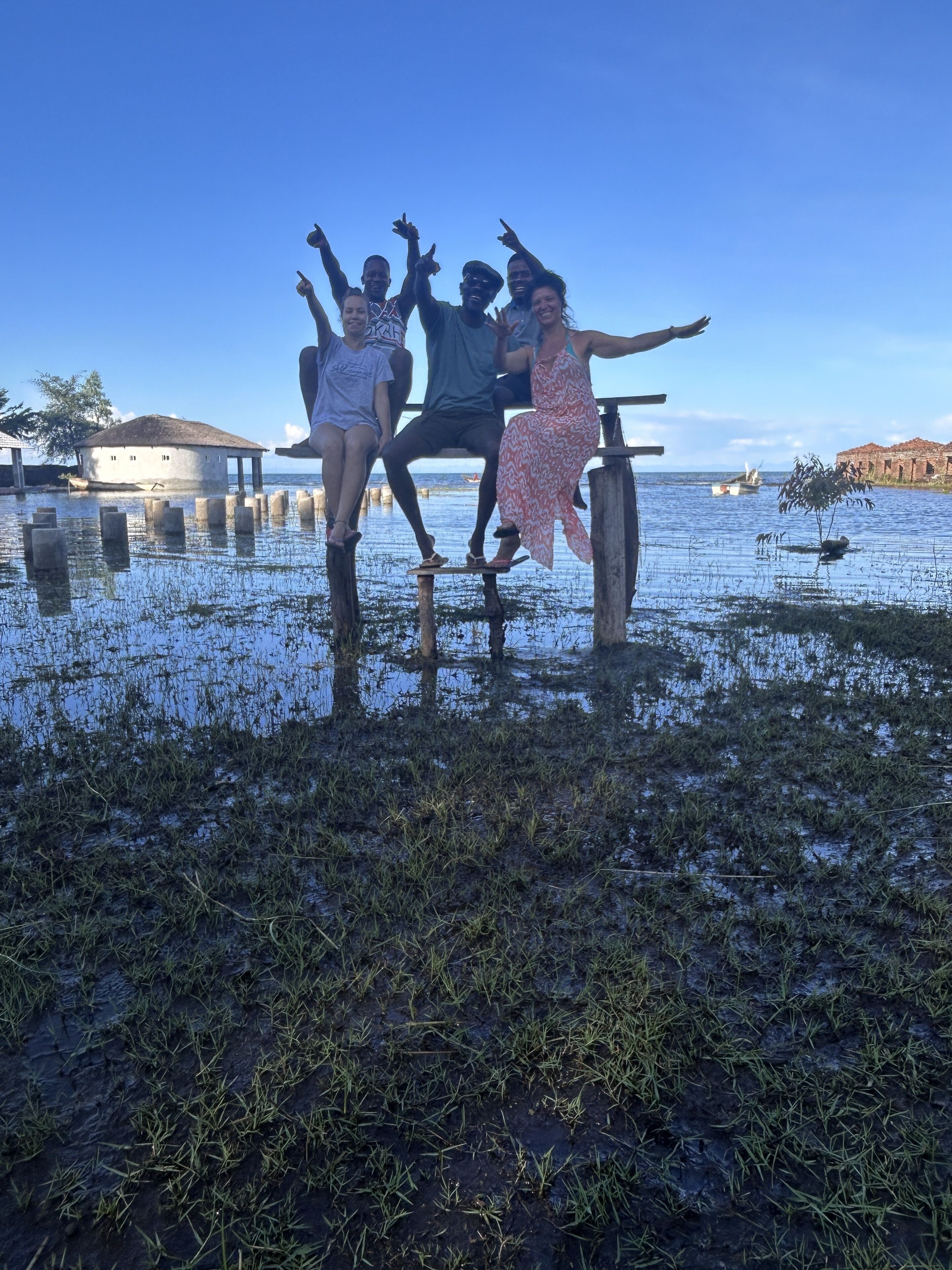 A group of people standing on stilts in a flooded area with a clear sky and boats in the background.