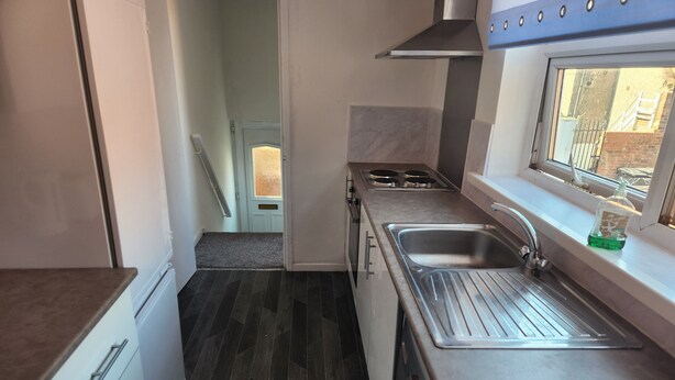 A compact kitchen with a built-in oven, a stainless steel sink, and a window overlooking a brick wall. - Inviting 3-bed House in Newcastle Upon Tyne (Newcastle-upon-Tyne)