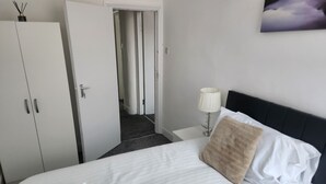A hotel room with a bed, a nightstand, a lamp, a door, and a wall-mounted picture. - Inviting 3-bed House in Newcastle Upon Tyne (Newcastle-upon-Tyne)