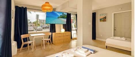 A hotel room with a bed, a desk, a chair, a TV, and a view of the beach.