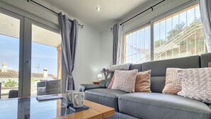 Ein modernes Wohnzimmer mit einem grauen Sofa, zwei Kissen, einem Couchtisch und einem Fenster mit Vorhängen.