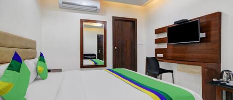 Habitación de hotel con cama, televisor montado en la pared, escritorio y equipo de aire acondicionado.