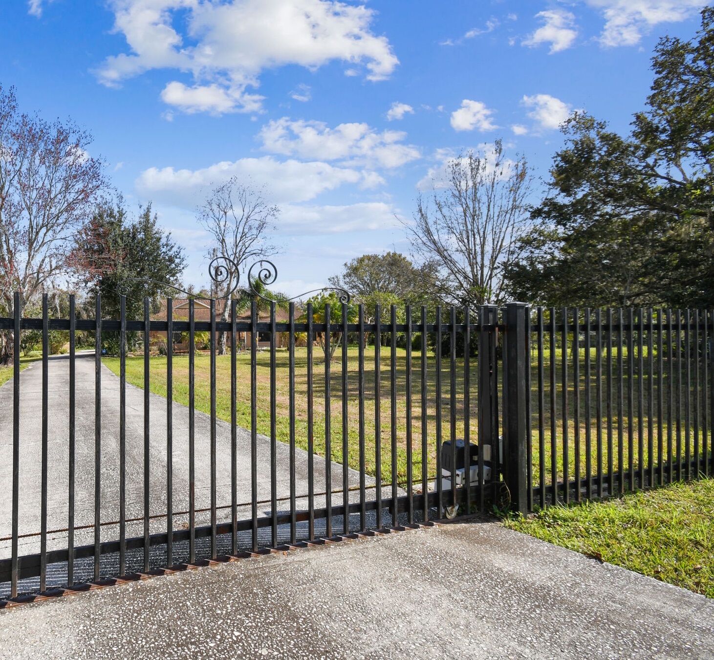 A gated area with a paved walkway leading to a grassy field.