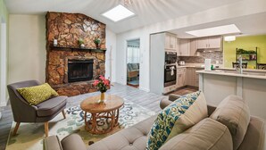 A modern living room with a stone fireplace, a dining area, and a kitchen with a bar. - TRANQUILITY. Gated Estate Home. Privacy. (Kissimmee)