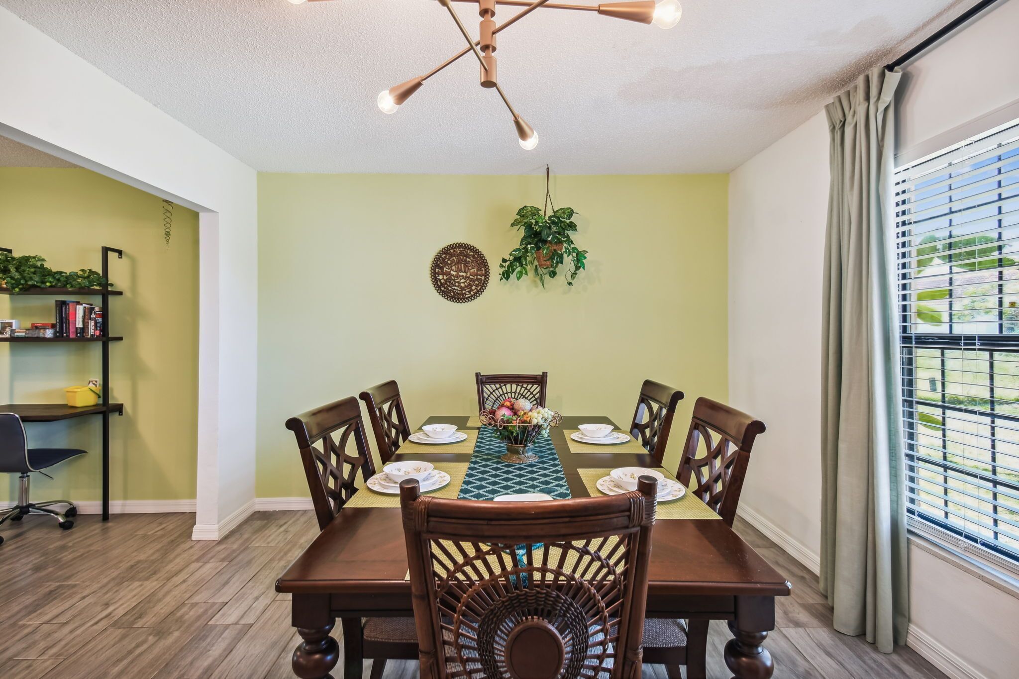 A dining area with a wooden table set for four, surrounded by chairs, a hanging plant, and a wall-mounted decorative item.