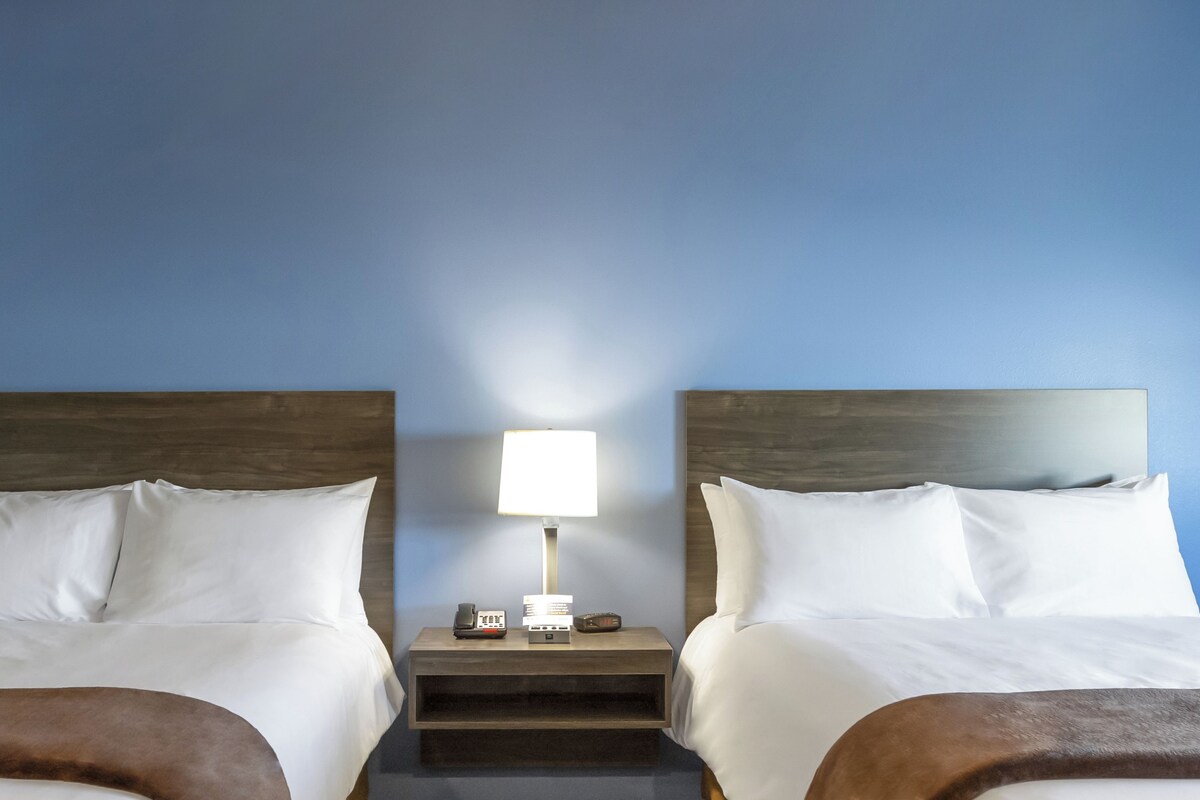 Una habitación de hotel con dos camas, una mesita de noche con lámpara y teléfono.