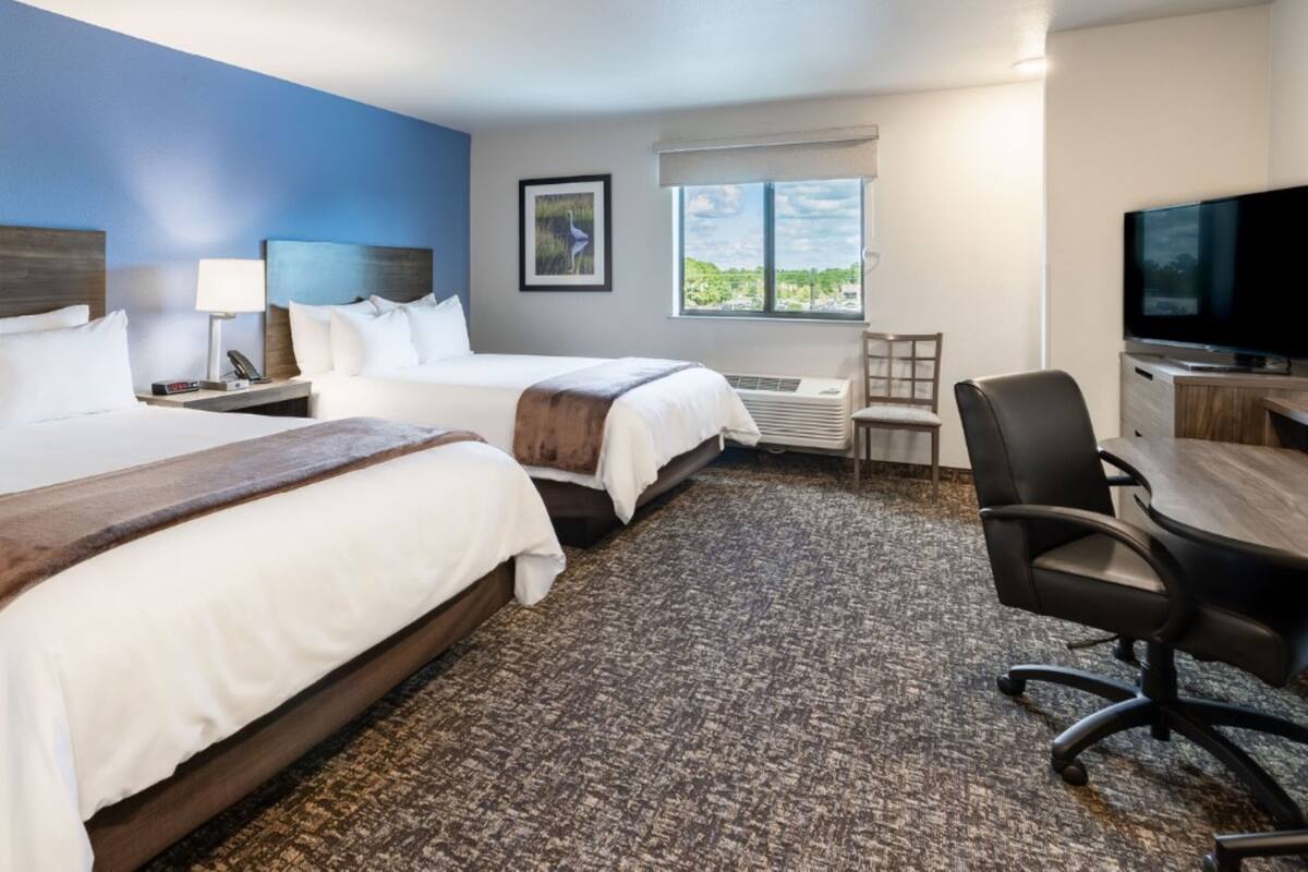 A hotel room with two beds, a desk, a chair, a TV, a window with a view, and a picture on the wall.