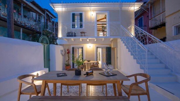 Uma casa de dois andares com varanda, escadaria e área de jantar com mesa e cadeiras.