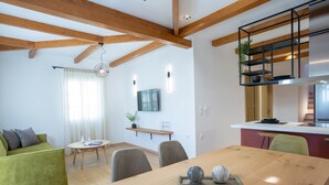 Sala moderna com mesa de jantar de madeira, sofá verde e área de cozinha com planta pendente.