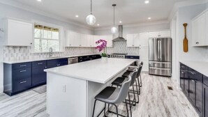 A modern kitchen with a large island, bar stools, stainless steel appliances, and pendant lighting.
