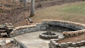 A stone fire pit surrounded by a stone wall in a landscaped area.