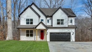 A two-story house with a garage, a red door, and a well-maintained lawn.
