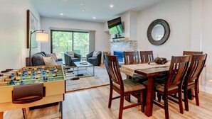 Uma sala de estar com mesa de futebol, uma área de jantar com cadeiras e mesa de madeira, e uma lareira.