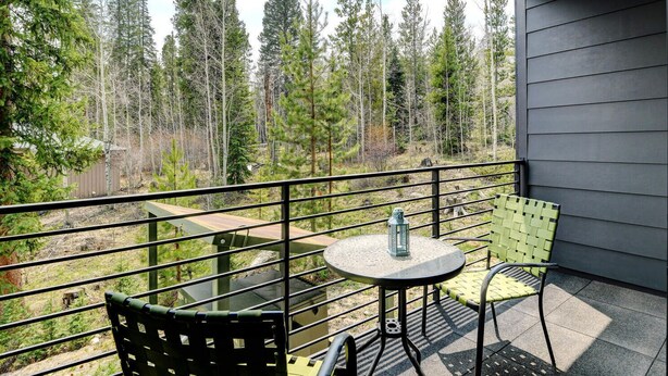 Varanda com mesa e cadeiras, com vista para uma área arborizada.