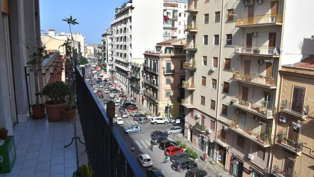 A busy urban street with multi-story buildings, parked cars, and potted plants on balconies. - Framamired (Palermo)