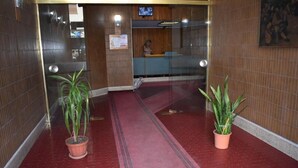A hotel reception area with a red carpet, wooden walls, and two potted plants. - Framamired (Palermo)