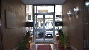 A hotel entrance with a glass door, potted plants, and a red carpet. - Framamired (Palermo)