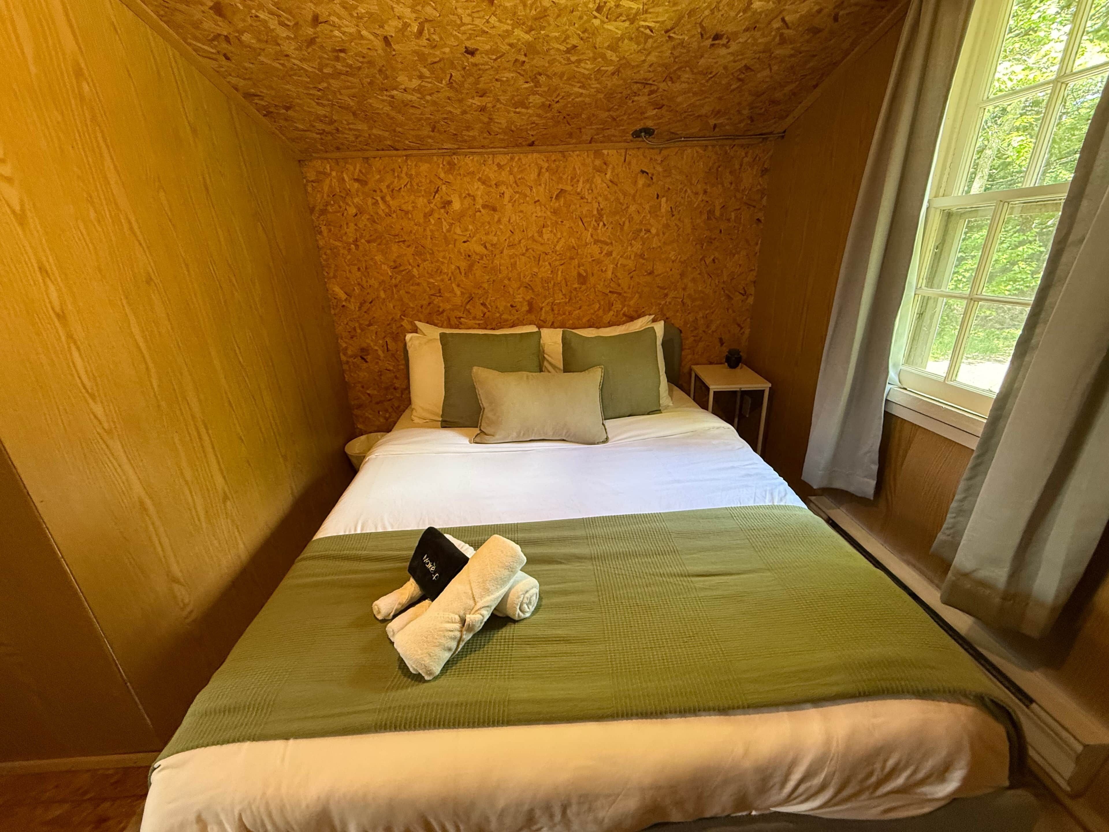 A room with a bed, pillows, a nightstand, and a window with curtains.