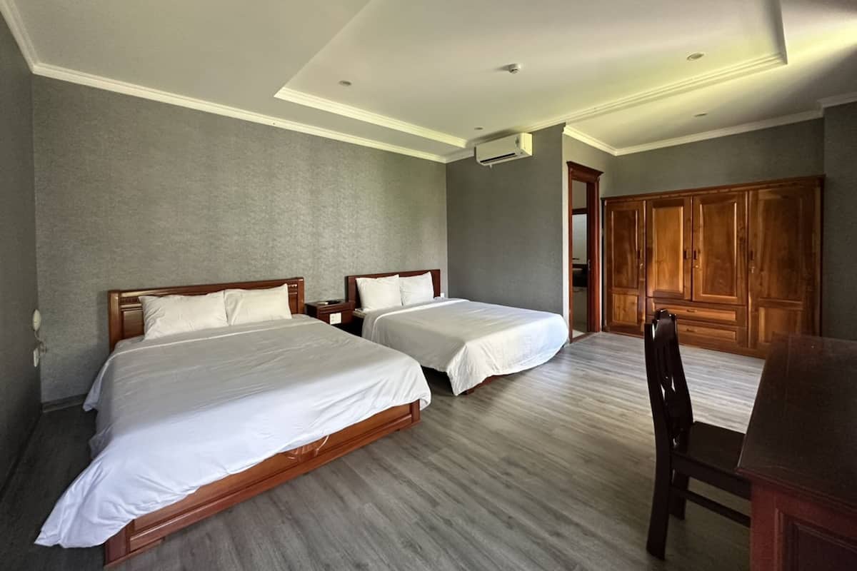 Una camera d'albergo con due letti, un armadio in legno, una scrivania e una sedia.