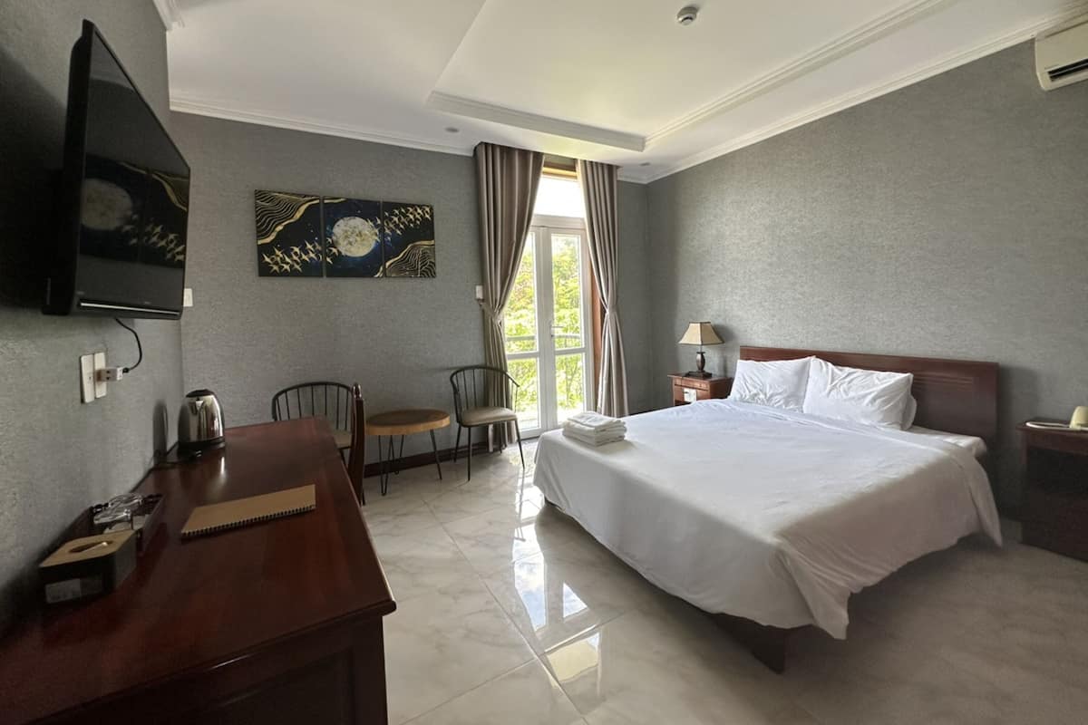 Una camera d'albergo con un letto, una scrivania, una sedia, una televisione e una finestra con tende.