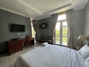 Een hotelkamer met een bed, een bureau met stoel, een televisie en een raam met gordijnen.