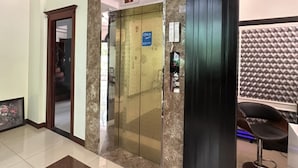 Un vestíbul amb sòl de marbre, una taquilla d'entrada, un ascensor de vidre i una paret amb un disseny decoratiu.