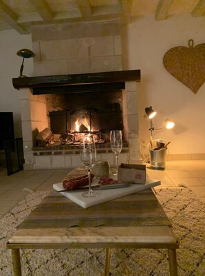 Um quarto acolhedor com lareira de pedra, uma mesa com garrafa de vinho, um copo e um prato de comida.